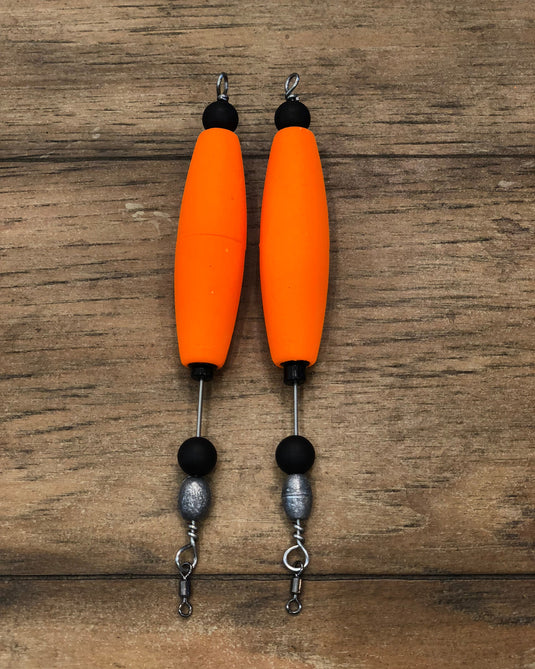 Two orange fishing corks with black and silver components on a cork surface.