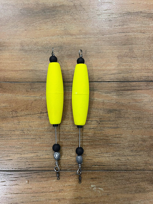 Two yellow fishing floats with black and silver attachments on a cork surface